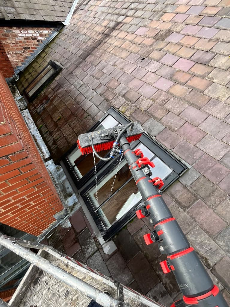 Water fed cleaning brush above roof windows beside an access platform