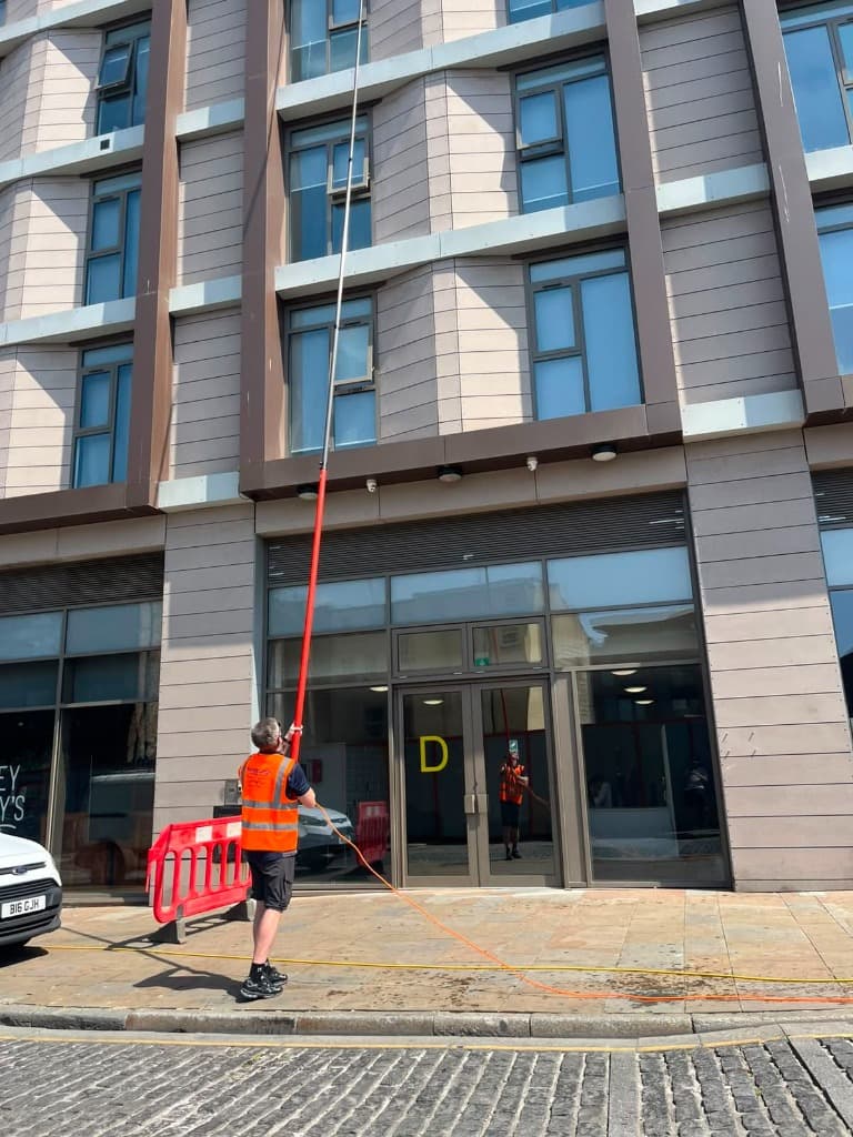 Operative in high visibility clothing cleaning entrance glazing on a panelled commercial building