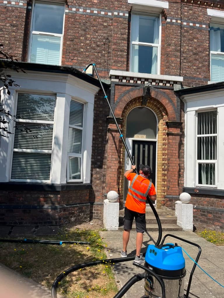 Window cleaner in high visibility clothing using a water fed pole on a Victorian terraced house