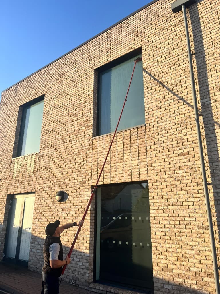Window cleaner using a water fed pole on an upper window of a brick house