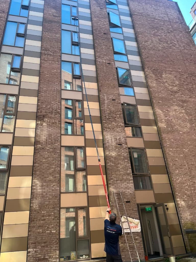 Operative using a Reach & Wash pole to clean upper floor windows on a brick building.